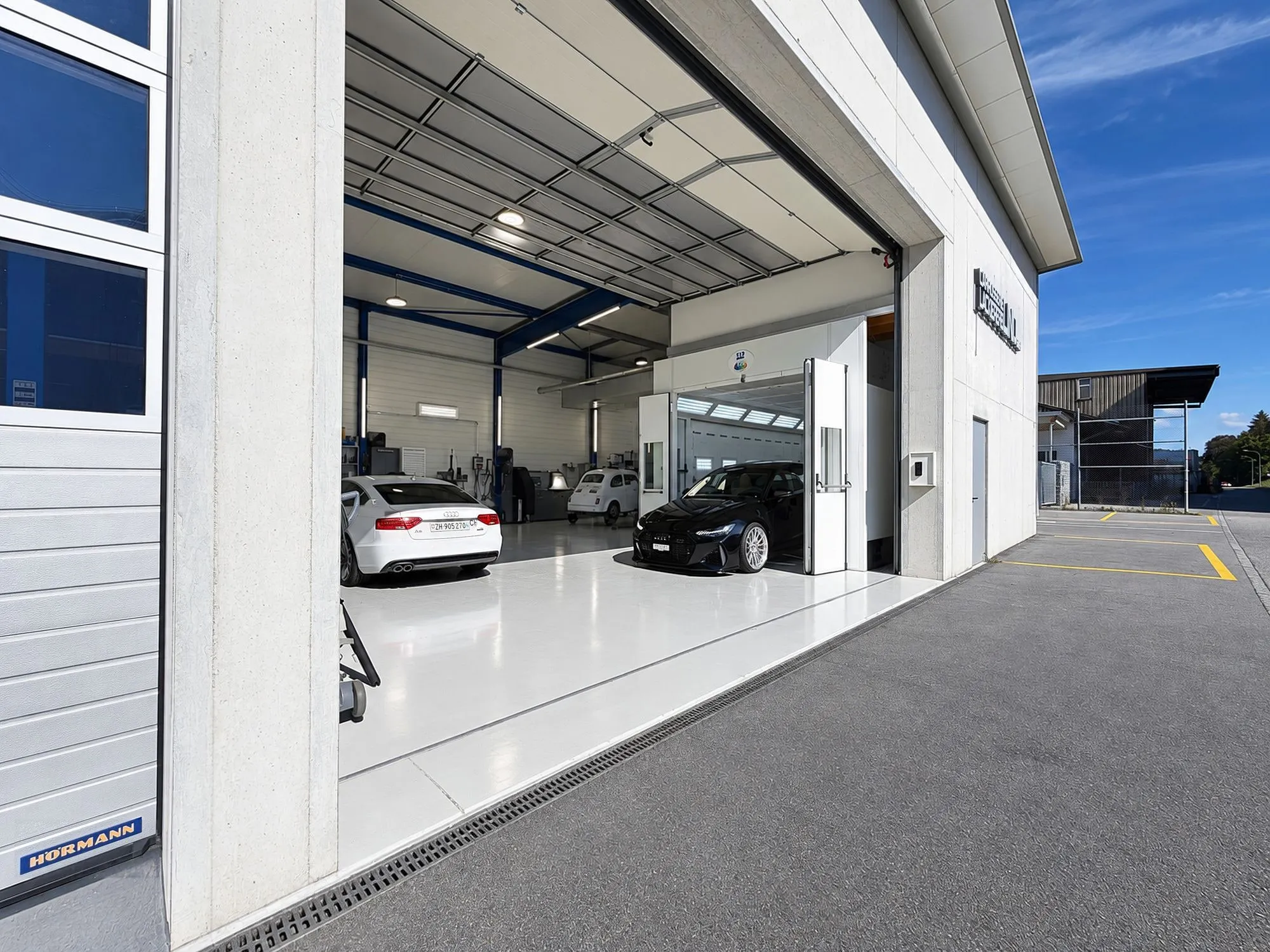 Offenes Werkstatttor, dahinter zwei Autos in der hellen Halle