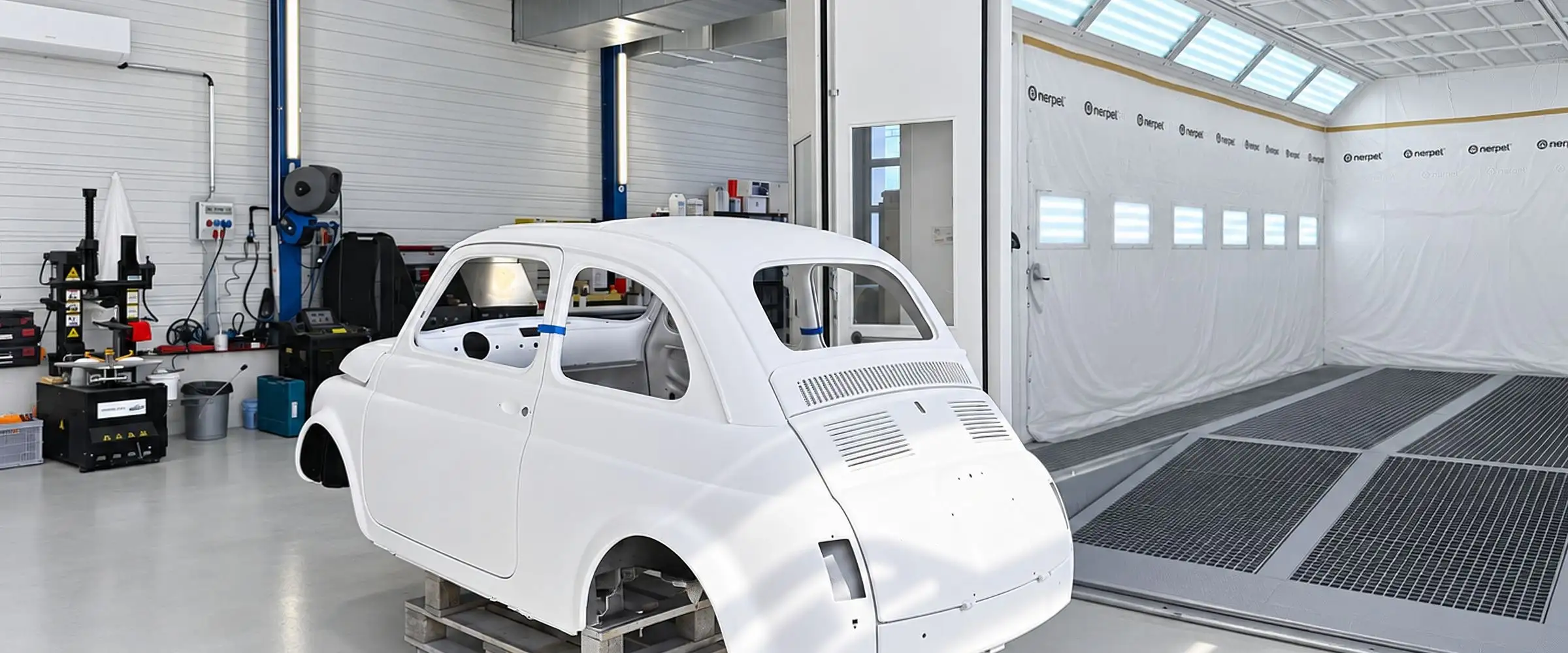Weisse Rohcarrosserie eines Fiat 500 auf einem Gestell vor der Spritzkabine