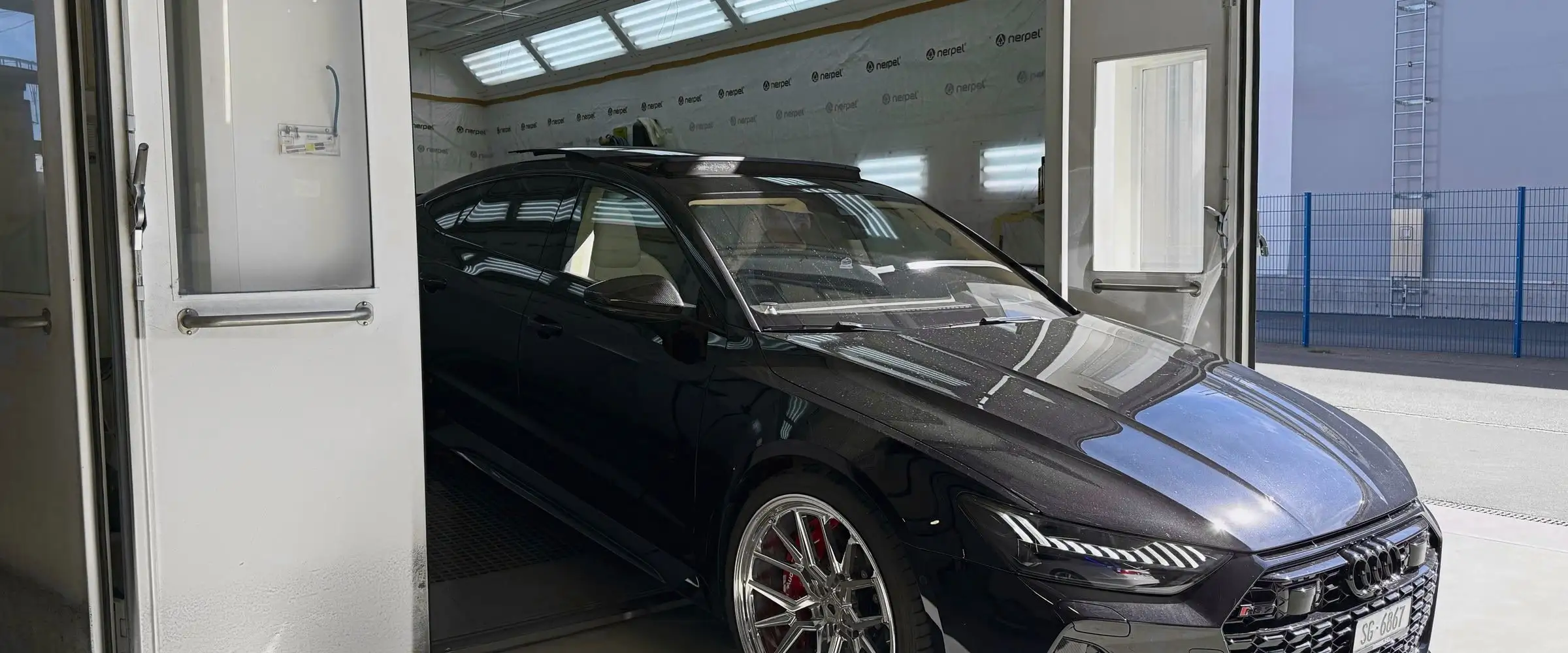 Schwarzer Audi RS7 mit glänzendem Lack vor der geöffneten Spritzkabine