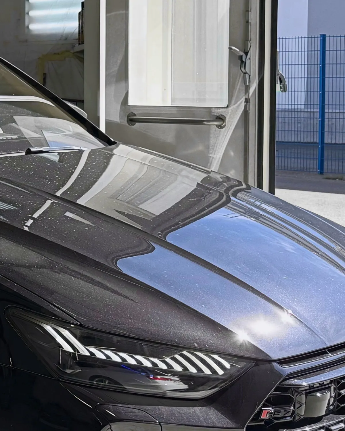 Schwarzer Metalliclack einer Motorhaube, in dem sich das Tageslicht spiegelt