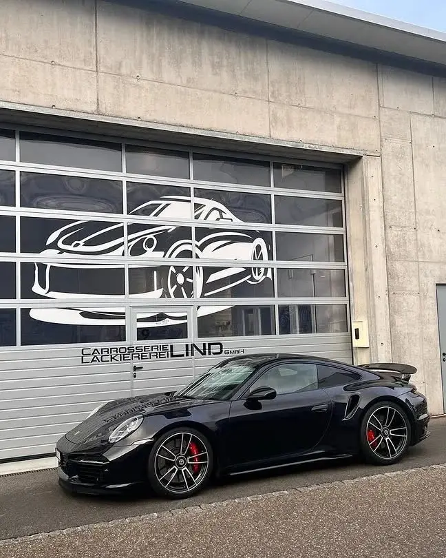 Schwarzer Porsche 911 vor dem Werkstatttor mit dem Lind-Schriftzug