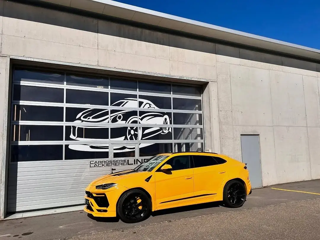 Gelber Lamborghini Urus vor dem Werkstatttor mit dem Lind-Schriftzug