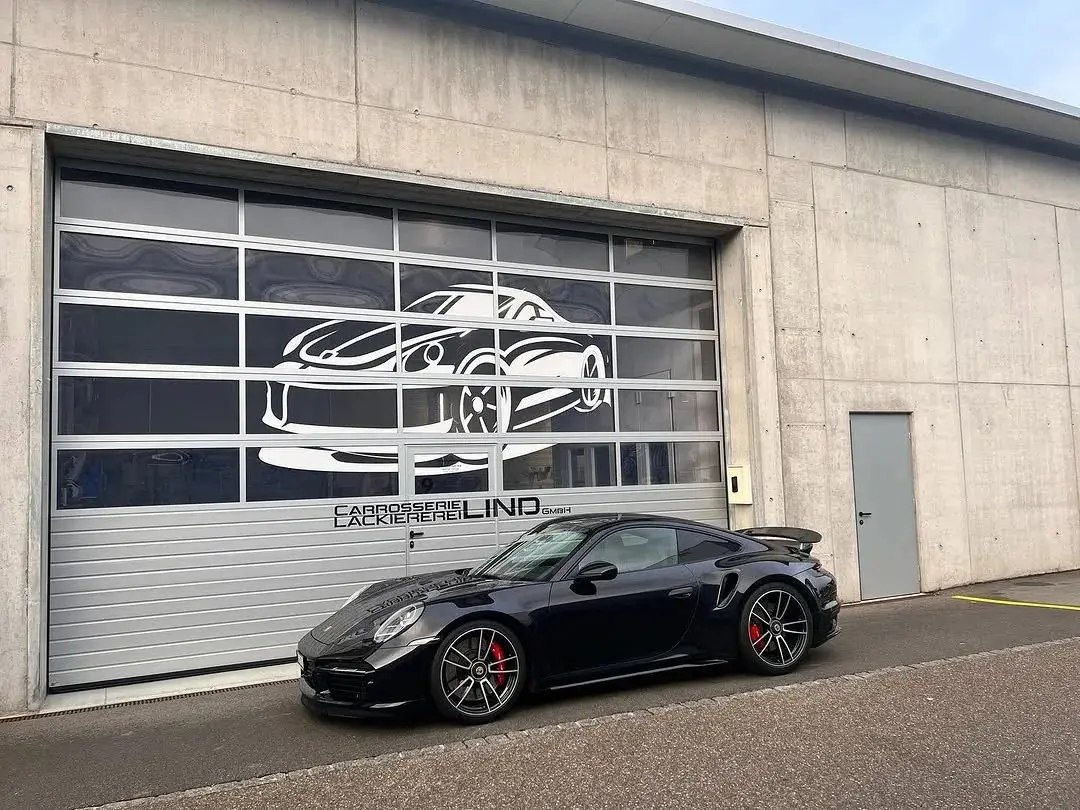 Schwarzer Porsche 911 vor dem Werkstatttor mit dem Lind-Schriftzug