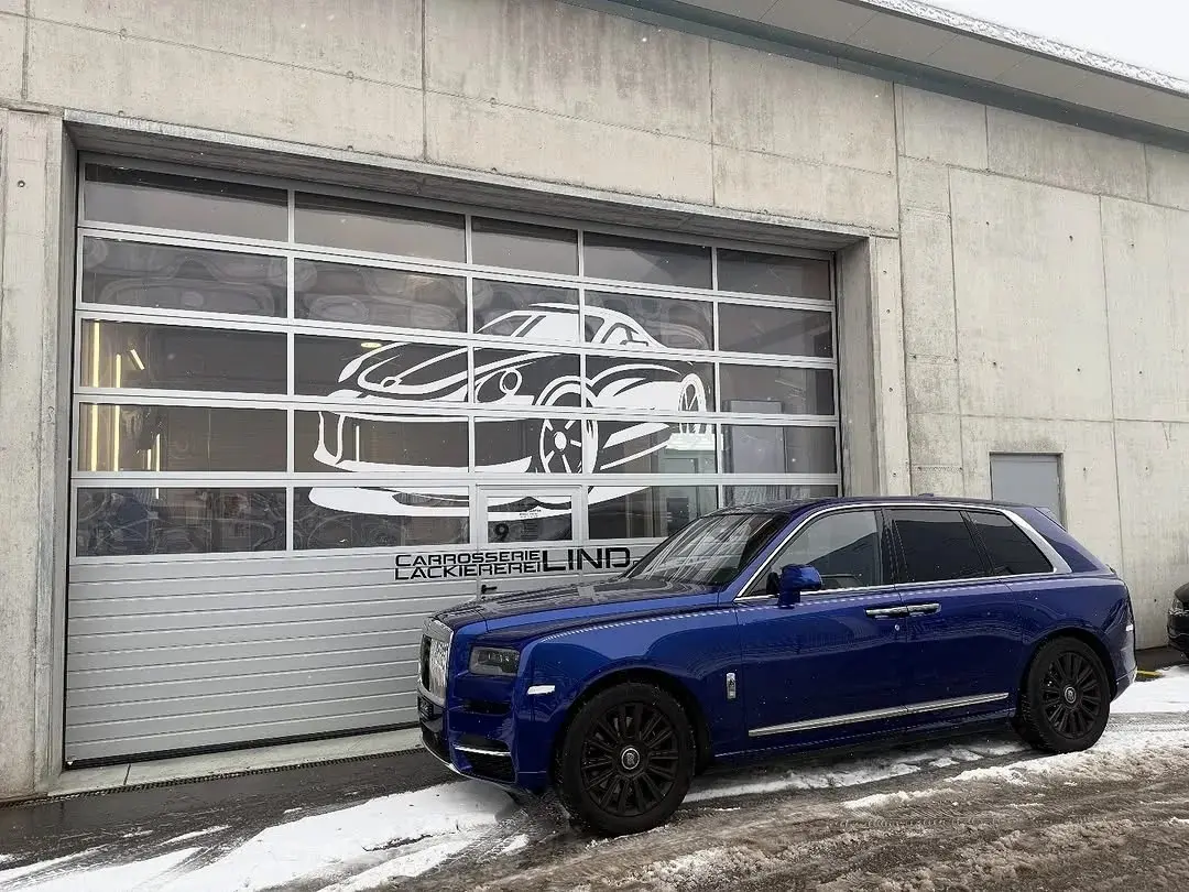 Blauer Rolls-Royce Cullinan vor dem Werkstatttor, Schnee am Boden